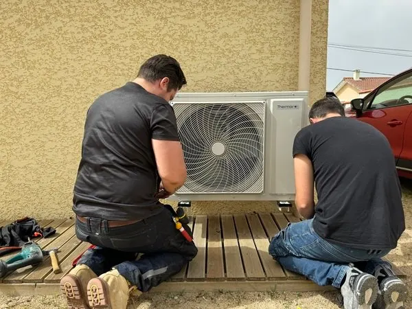 Deux techniciens posent une pompe à chaleur Thermor sur une terrasse en bois